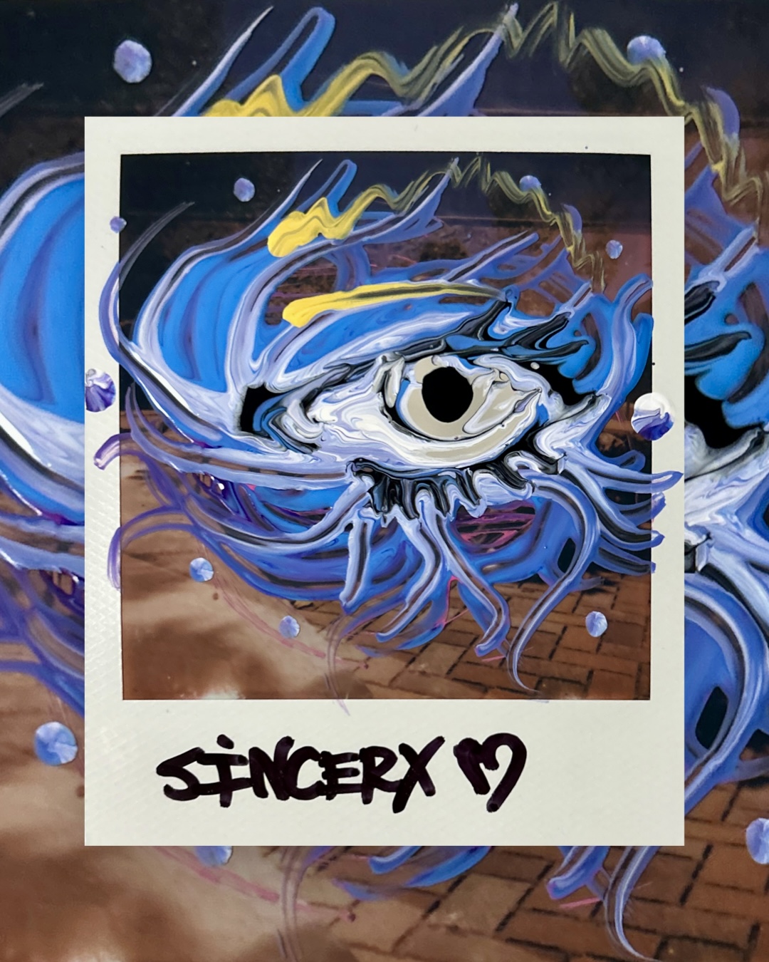 a large blue eye painted over a Polaroid of a brick walkway