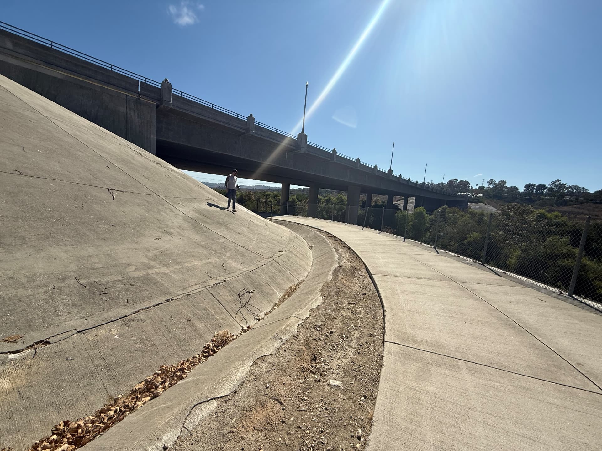Alberto photographing in a concrete flood-control channel under a bridge overpass in afternoon sun