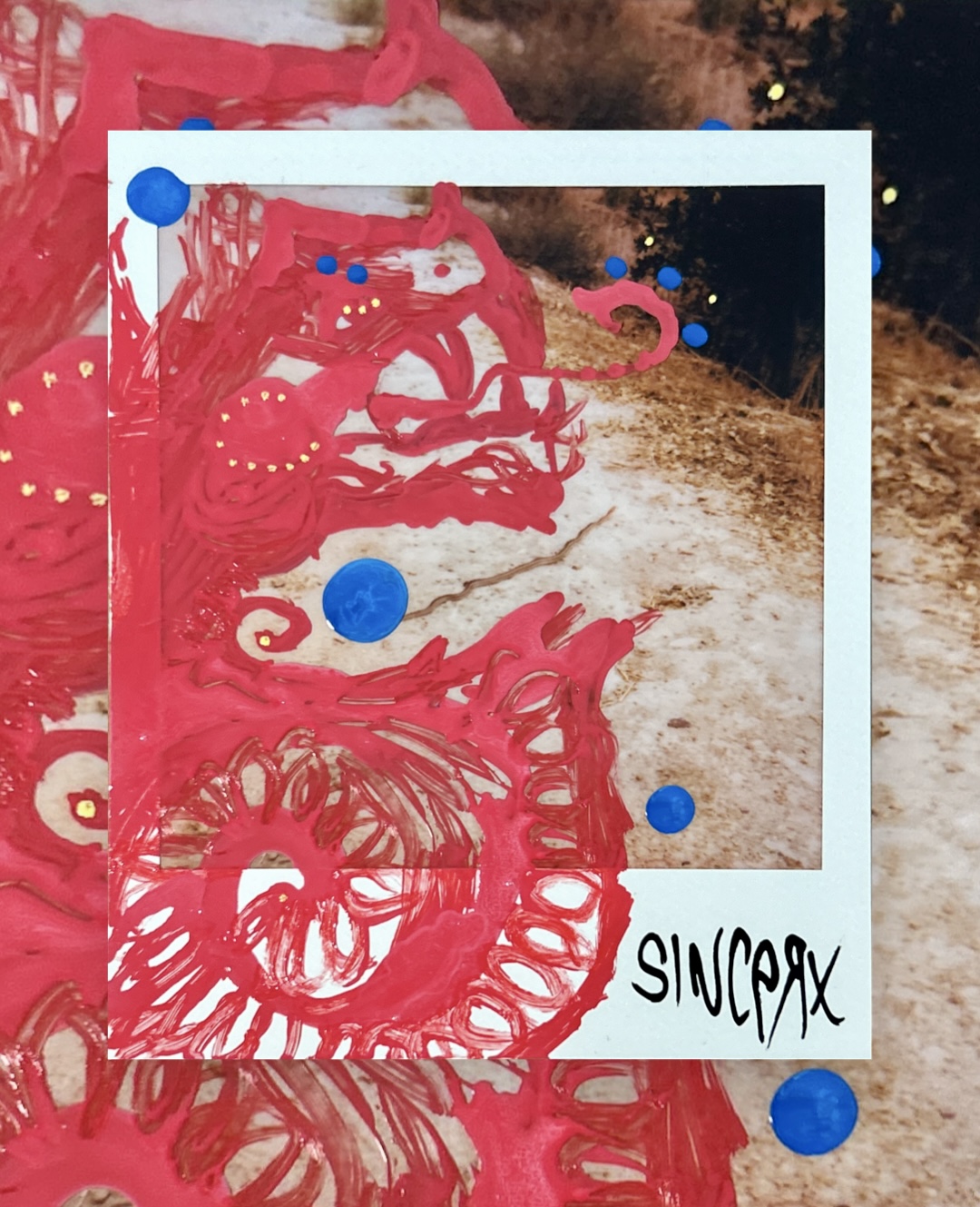 a red creature painted over a Polaroid of a dirt path, blue dots floating around it