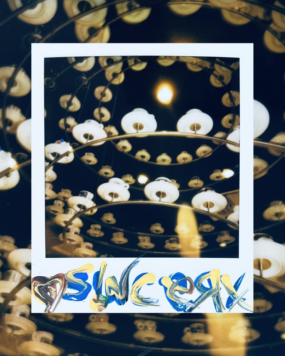 a Polaroid of a chandelier of white glass lampshades, signed sincerx in blue and yellow paint markers